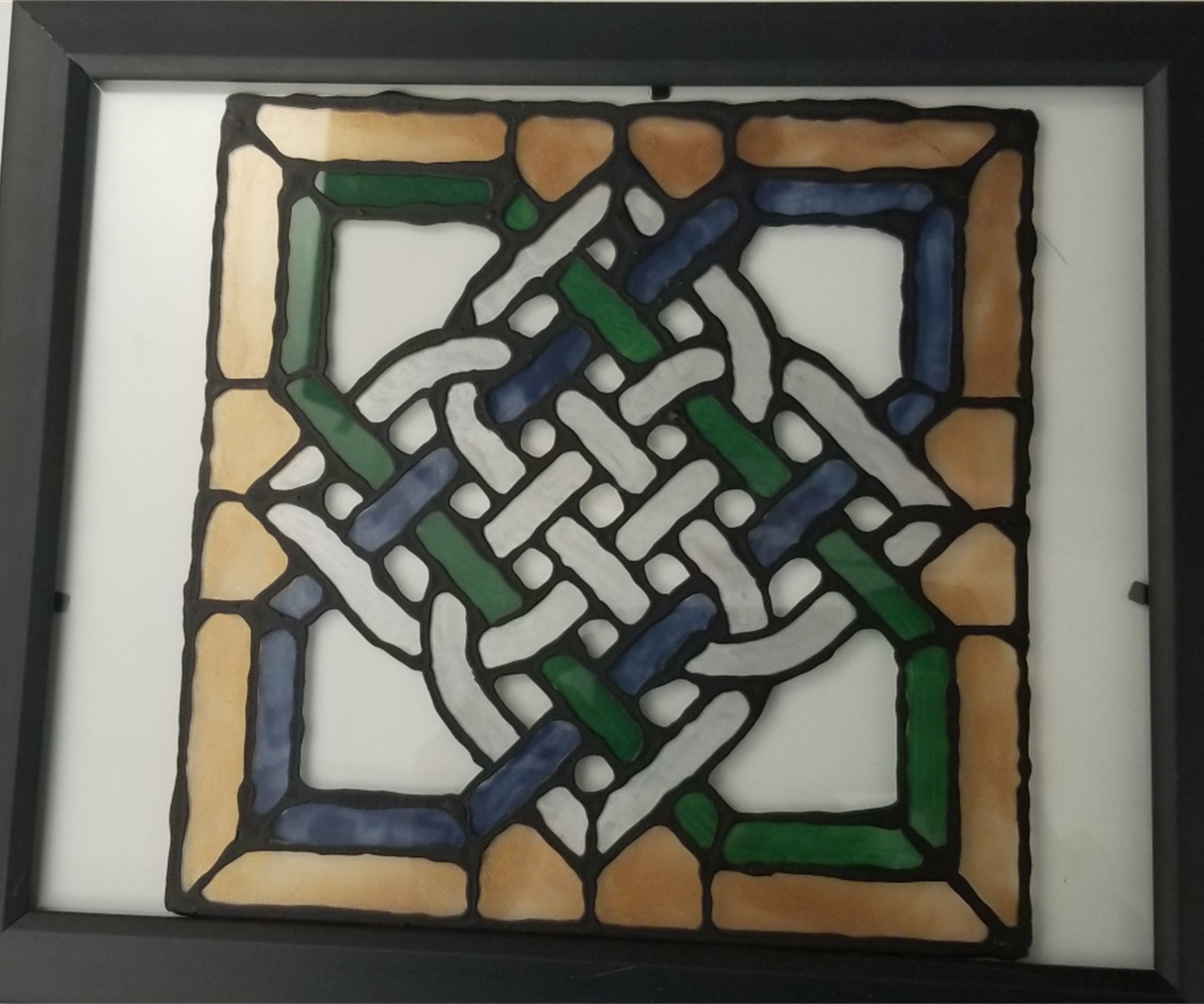 A green, gold, and white knotwork design on glass