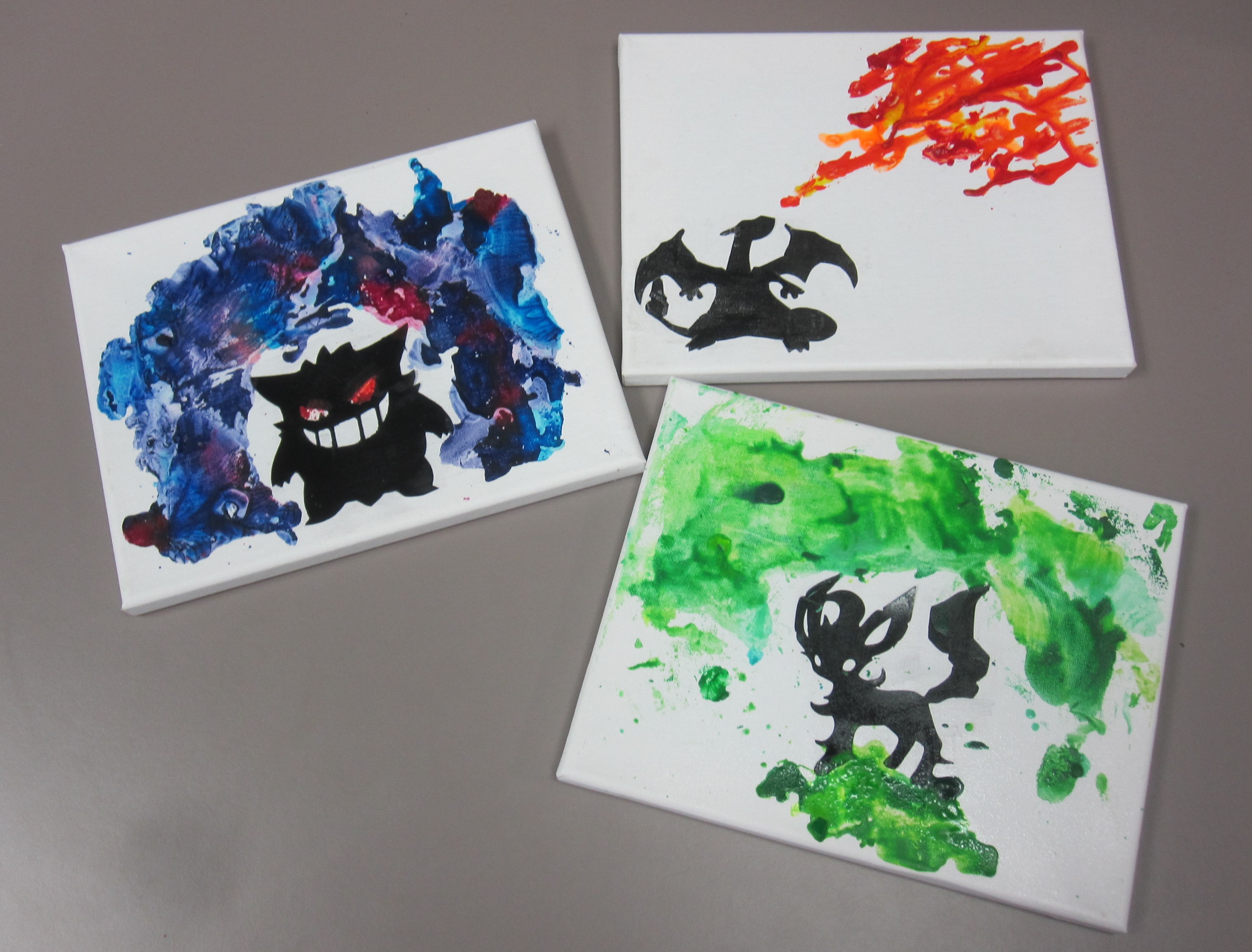 3 white canvas with silhouettes of Gengar, Charizard, and Leafeon surrounded by melted crayon