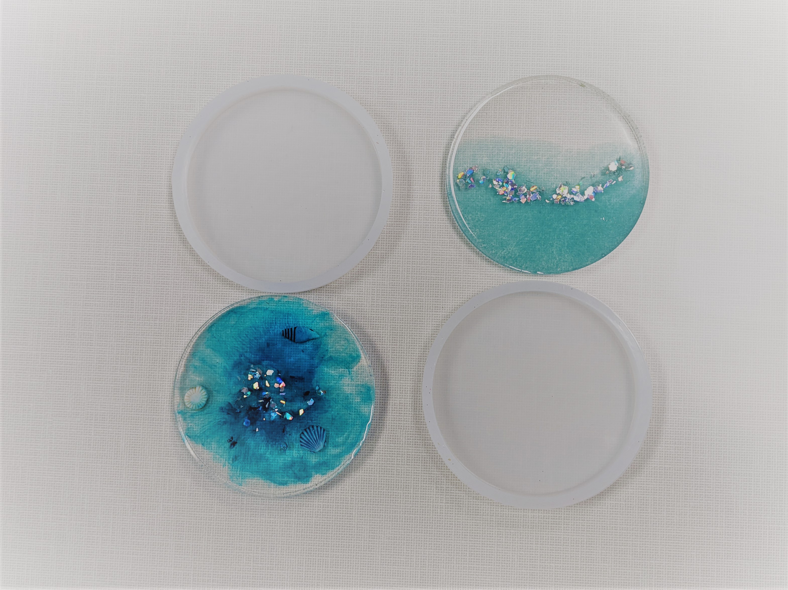 resin coaster with blue color, glitter, and shells, silicone modes, and second resin coaster half blue and half clear with glitter