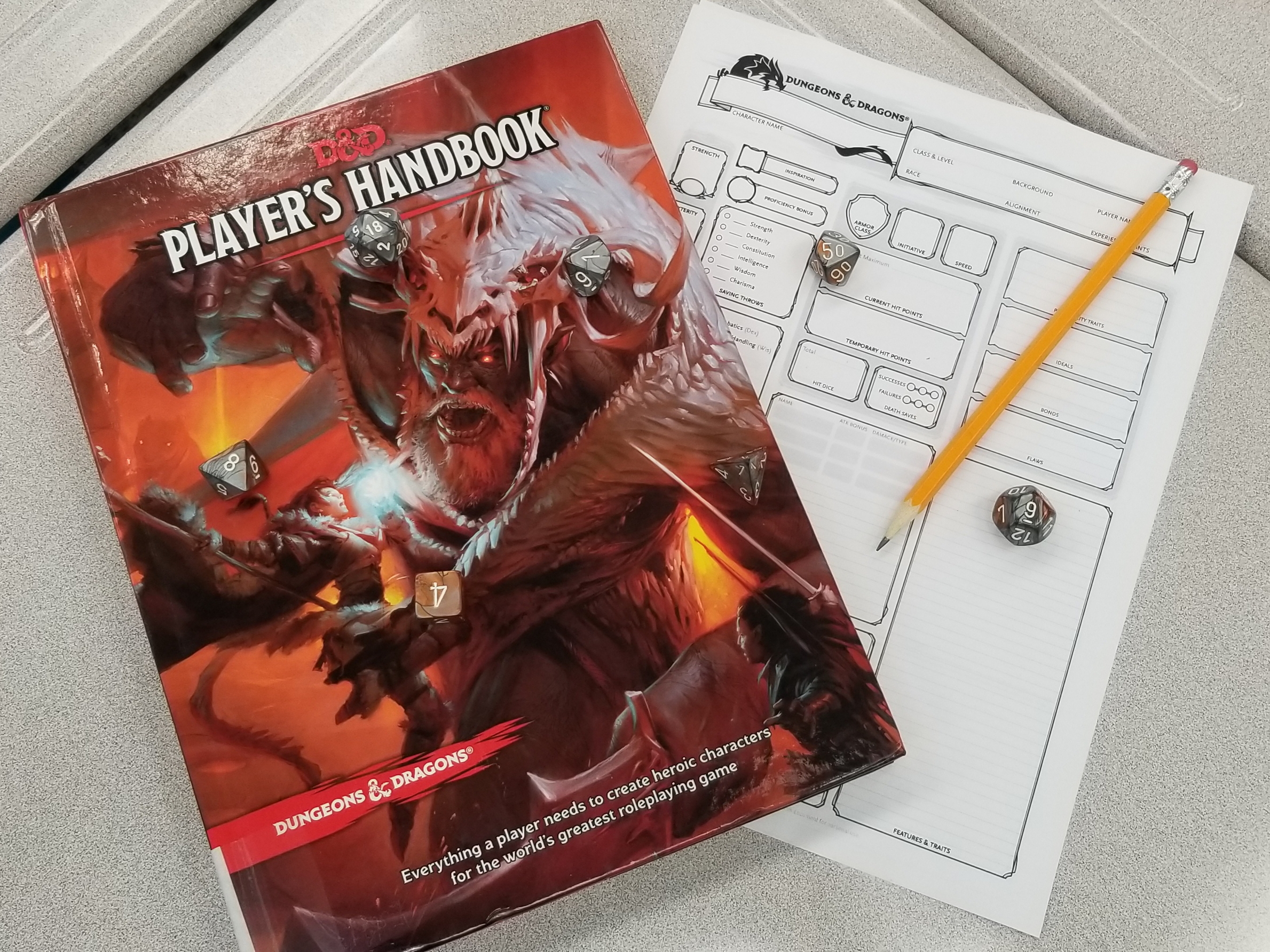 Picture of Dungeons & Dragons Player Handbook, a blank character sheet, dice, and a pencil 
