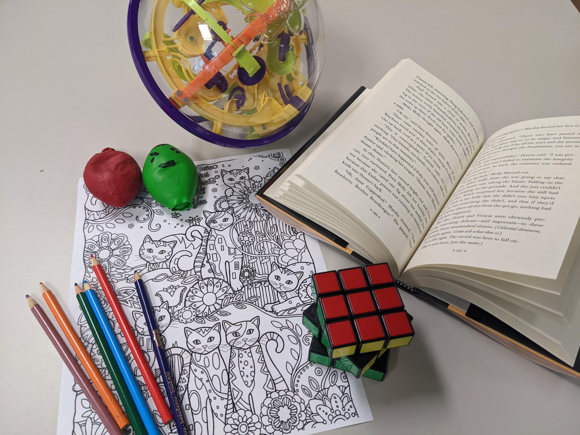 cat coloring sheet, color pencils, red and green stress ball, puzzle, Rubik's cube, and opened book