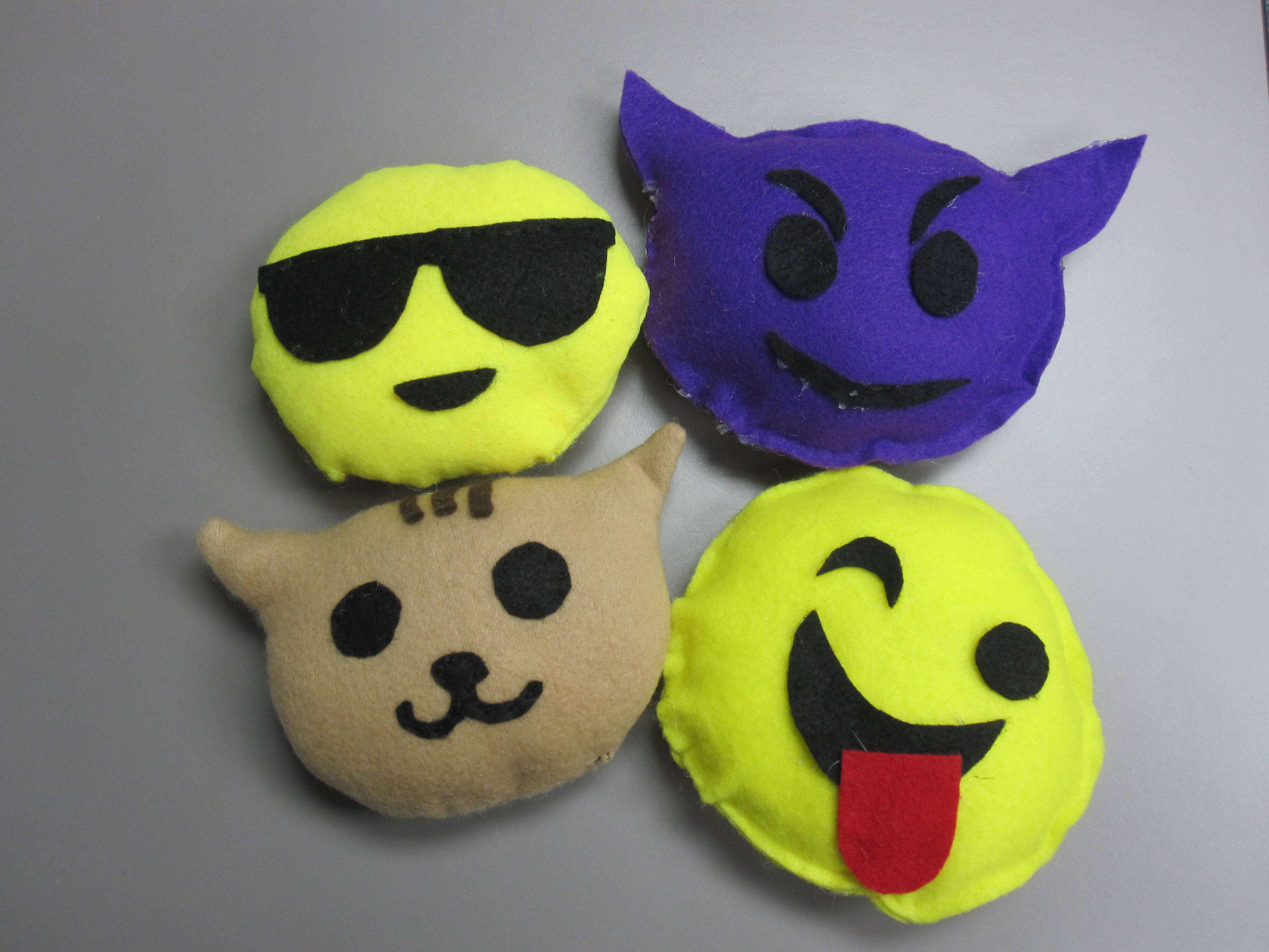 yellow emoji feltie with sunglasses, purple emoji with horns, brown cat emoji, and yellow emoji with tongue sticking out