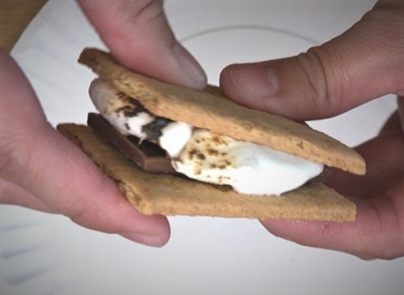 fingers holding s'mores (toasted marshmallow and chocolate sandwiched by graham crackers)