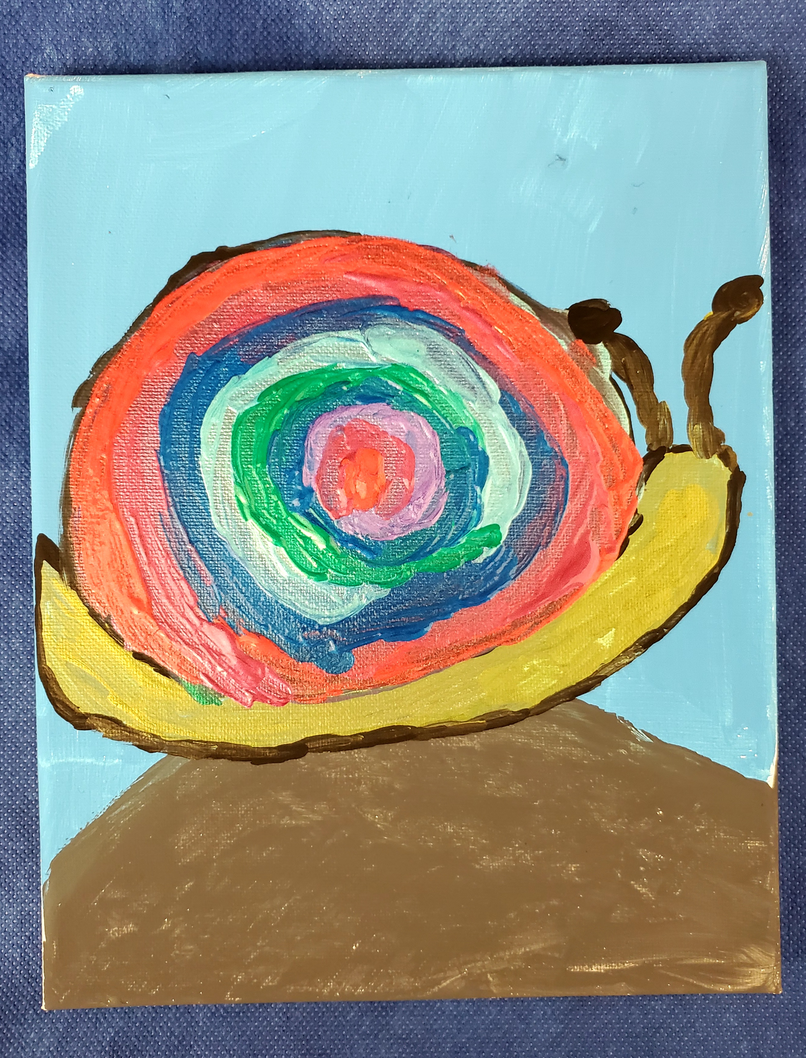 A lime green snail with a colorful shell (there are layers of pink, light pink, green, light blue, medium blue, orange, and red) sitting on a brown rock with a blue background.