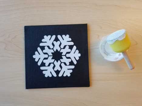 white snowflake on black canvas - sponge stippler brush with white paint on it and it's on top of a condiment cup that has white paint in it