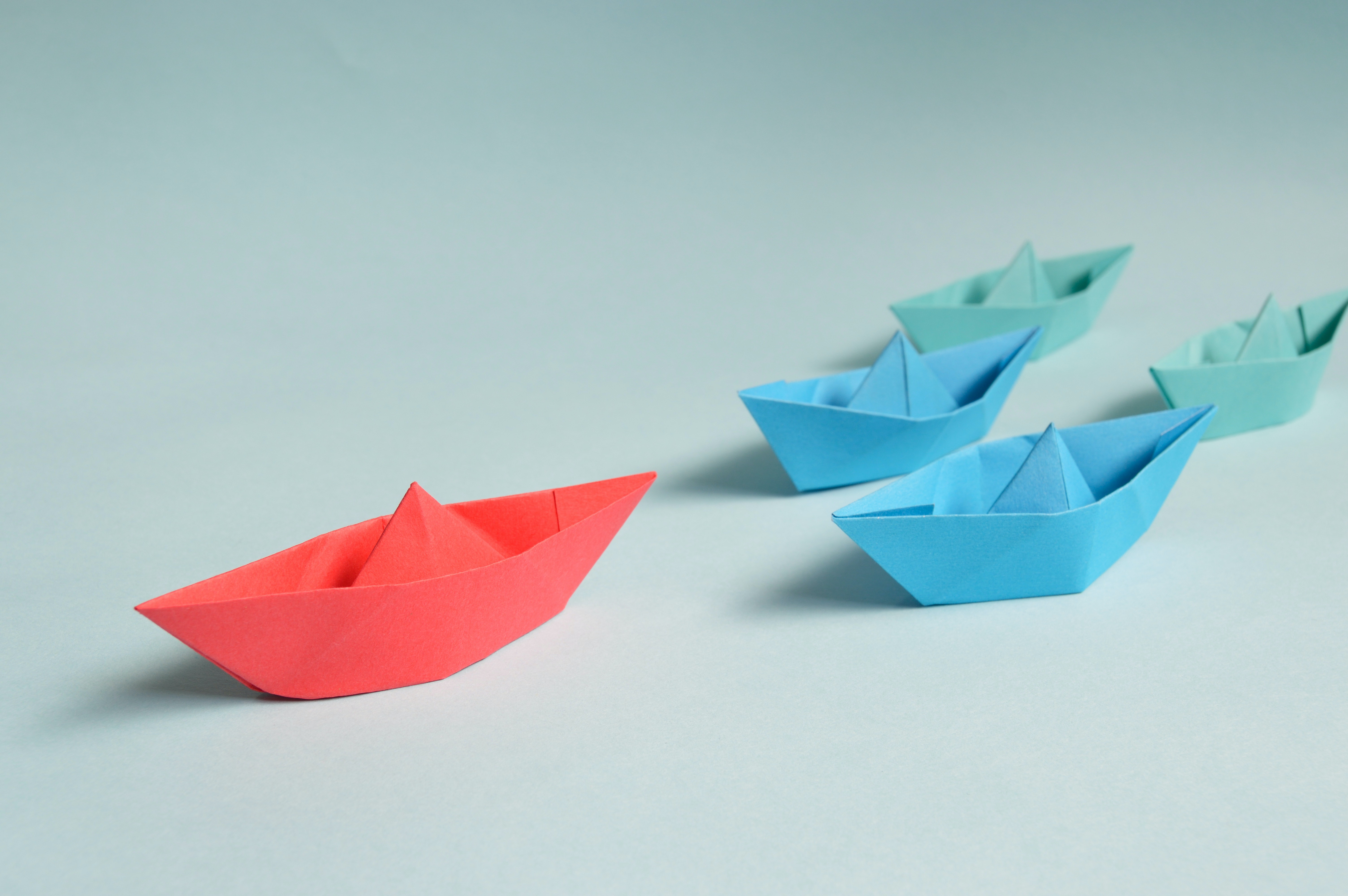 red origami boat, followed by two blue origami boats, and two light green origami boats