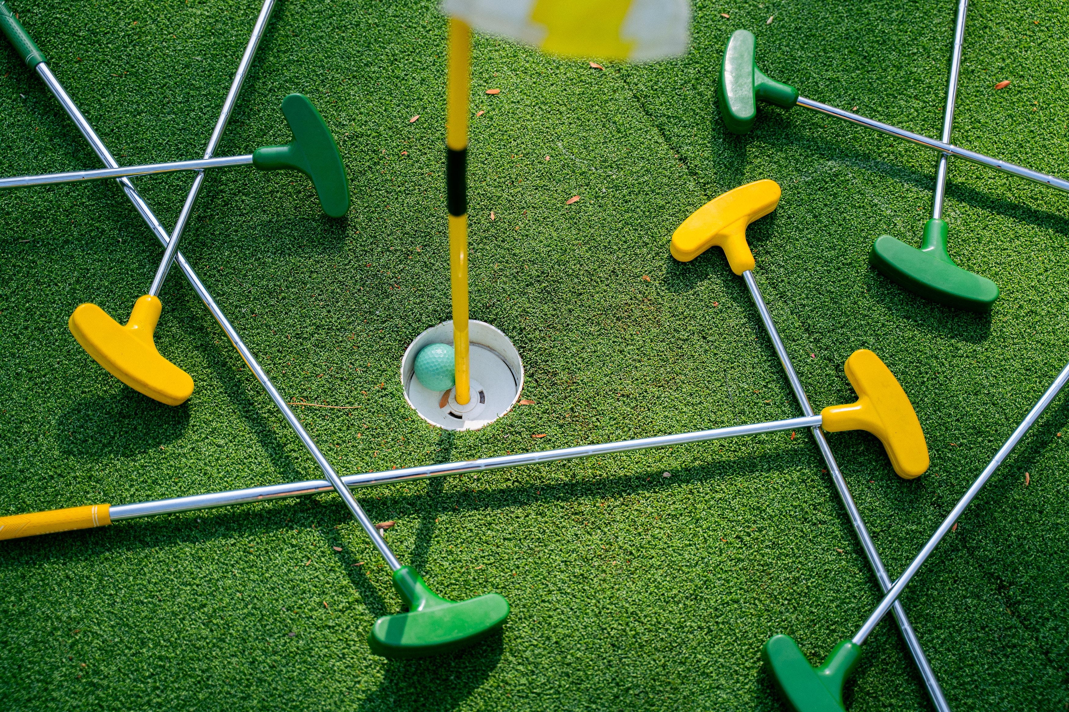 green background with yellow and green putters with golf ball in a hole