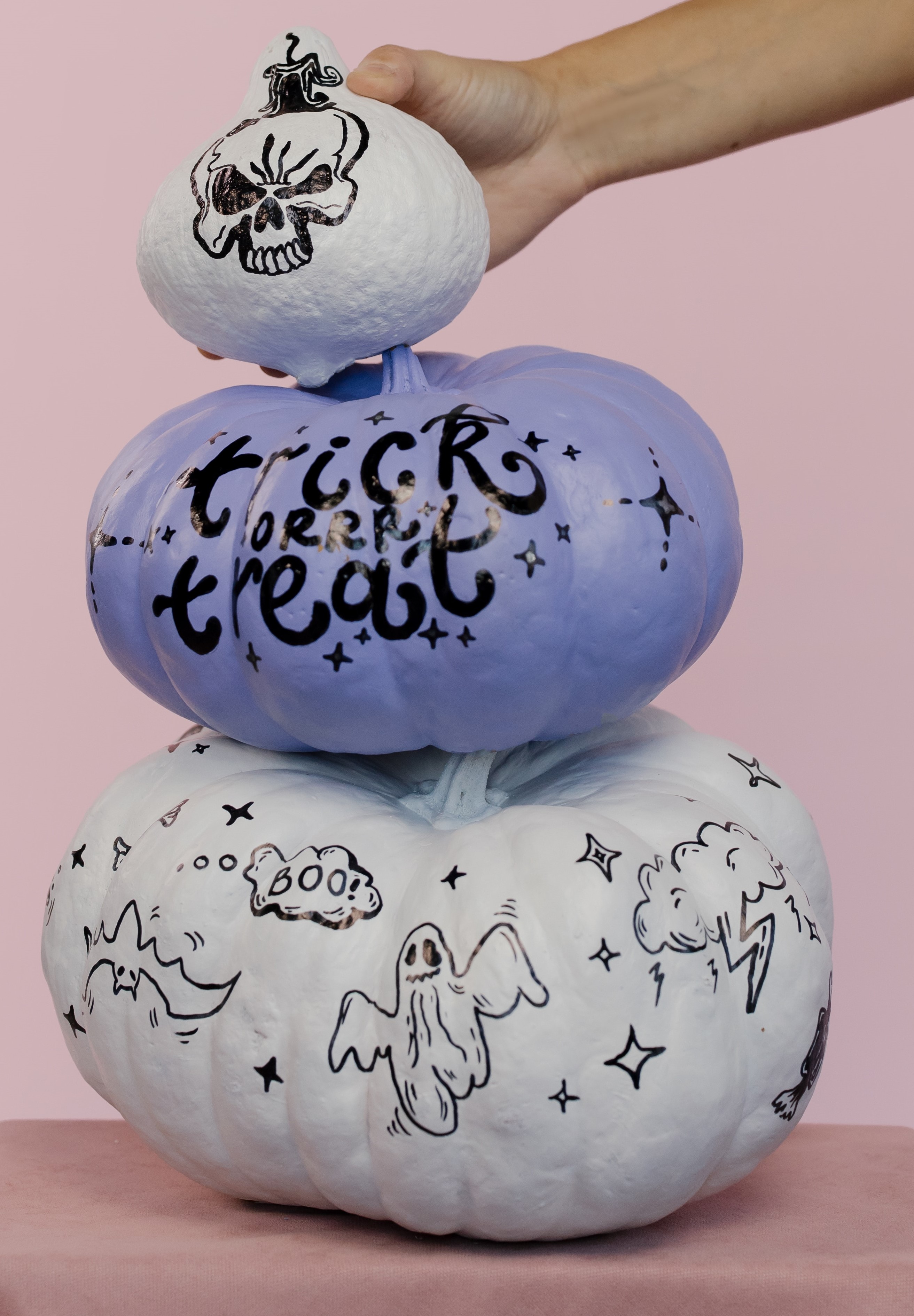 white pumpkin with skull, light purple pumpkin with "trick or treat," and white pumpkin with Halloween drawings all stacked
