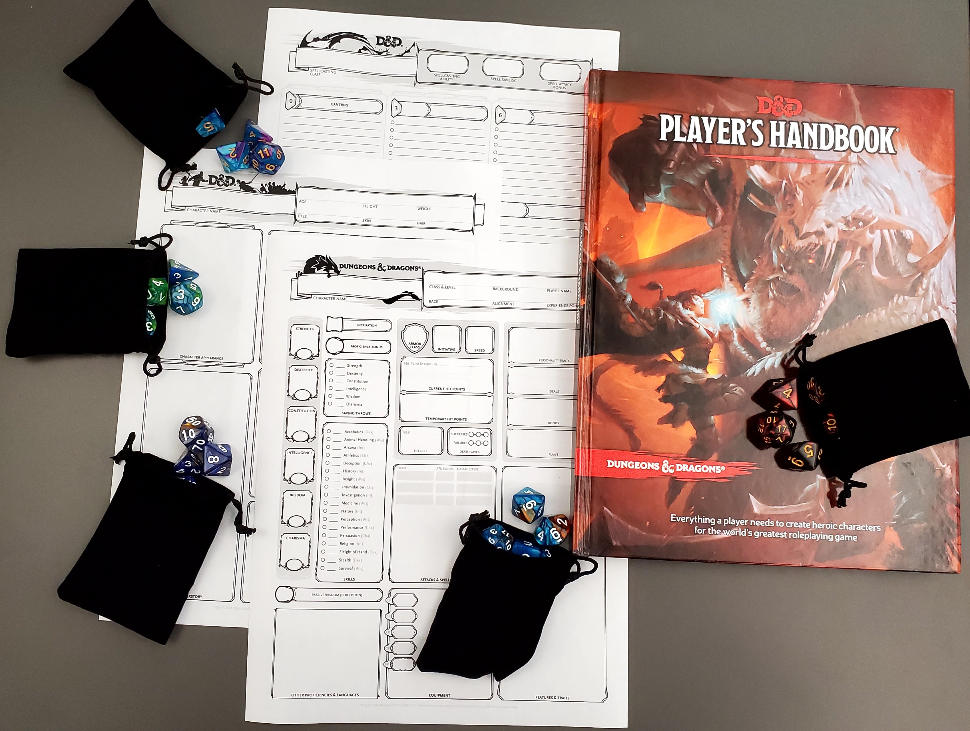 To the right: Dungeons and Dragons Players Handbook, a black bag of dice on top of the book, to the left there are 3 blank characters sheets and 4 black bags with colorful Dungeons and Dragons dice spilling out