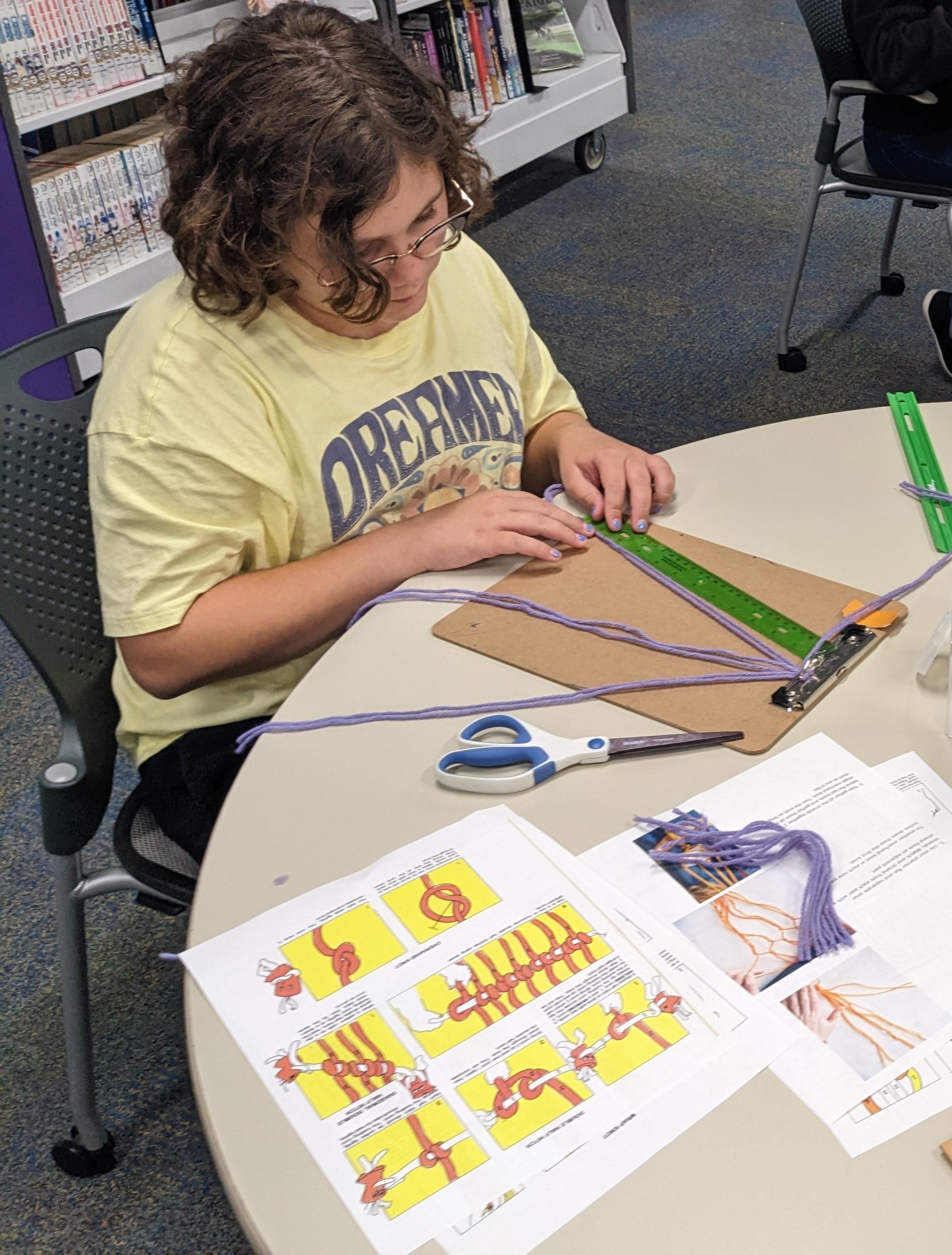 Teen in yellow shirt working with purple yarn to create a macramé project