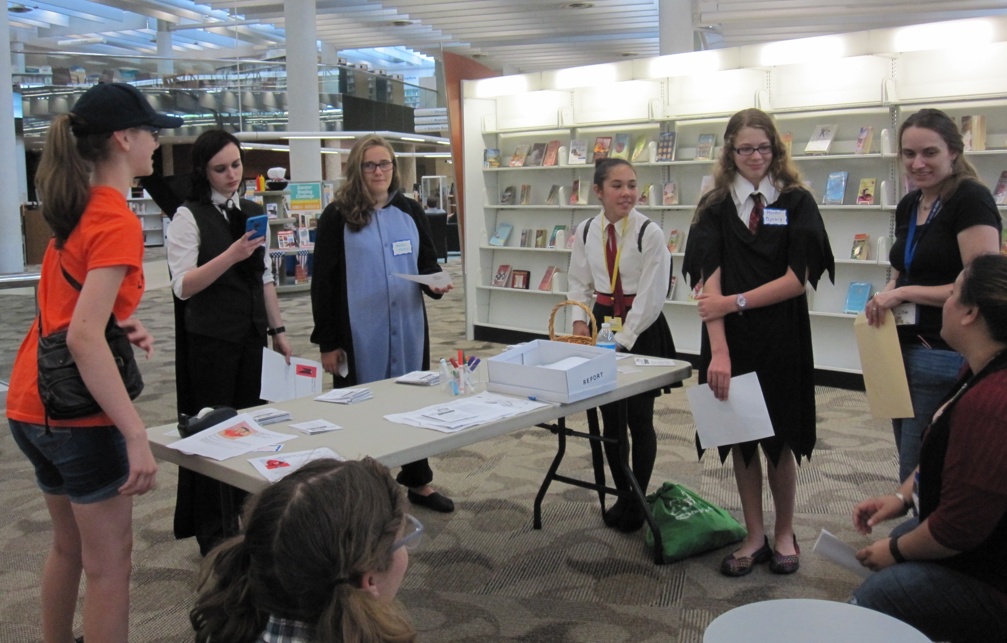 teens stand around a table at a murder mystery at the library