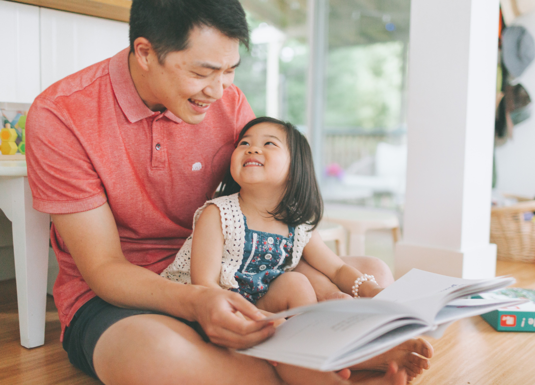 Father and daughter of Asian descent enjoying a picture book together.