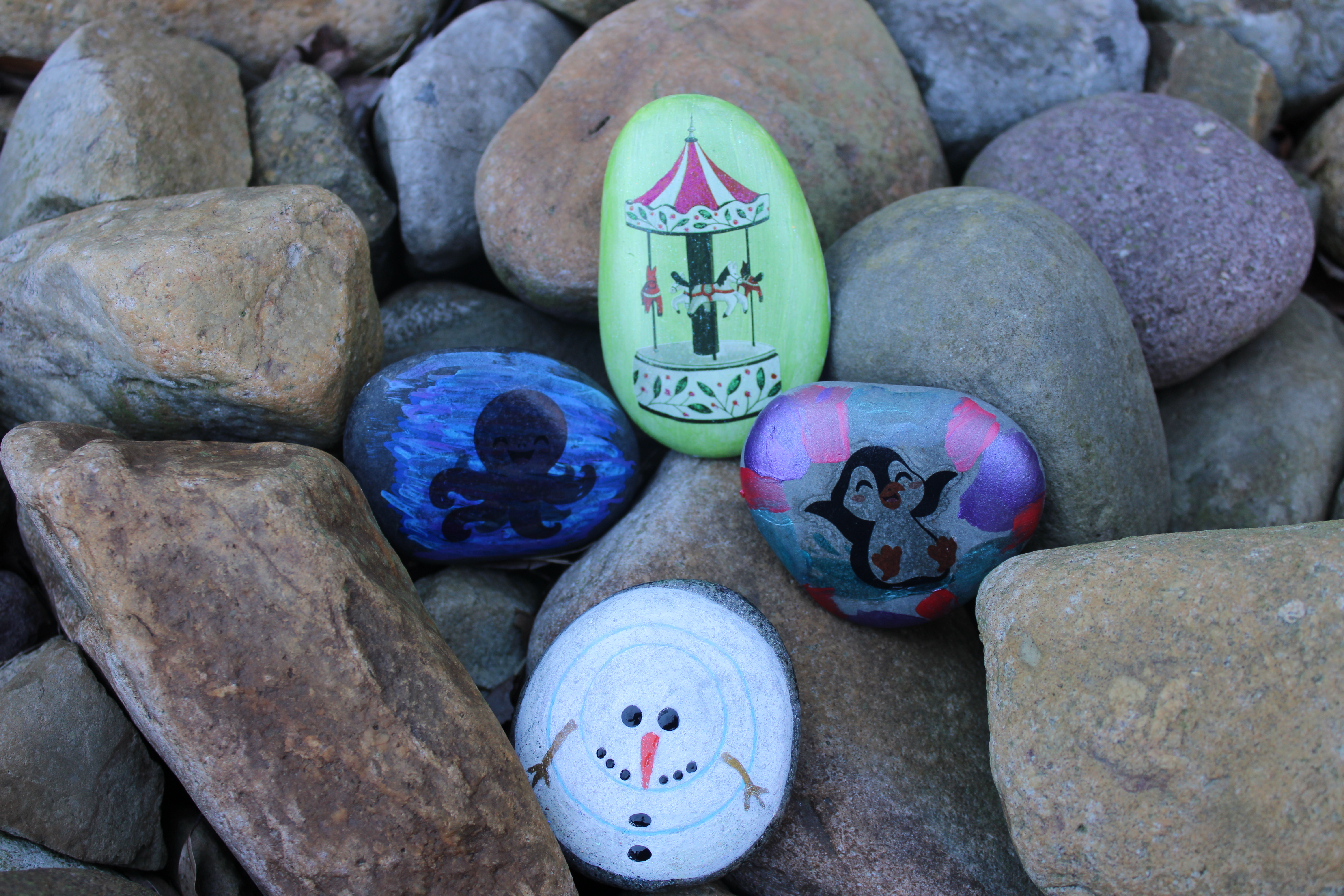 Four rocks decorated with paint and tattoo surrounded by plain rocks.
