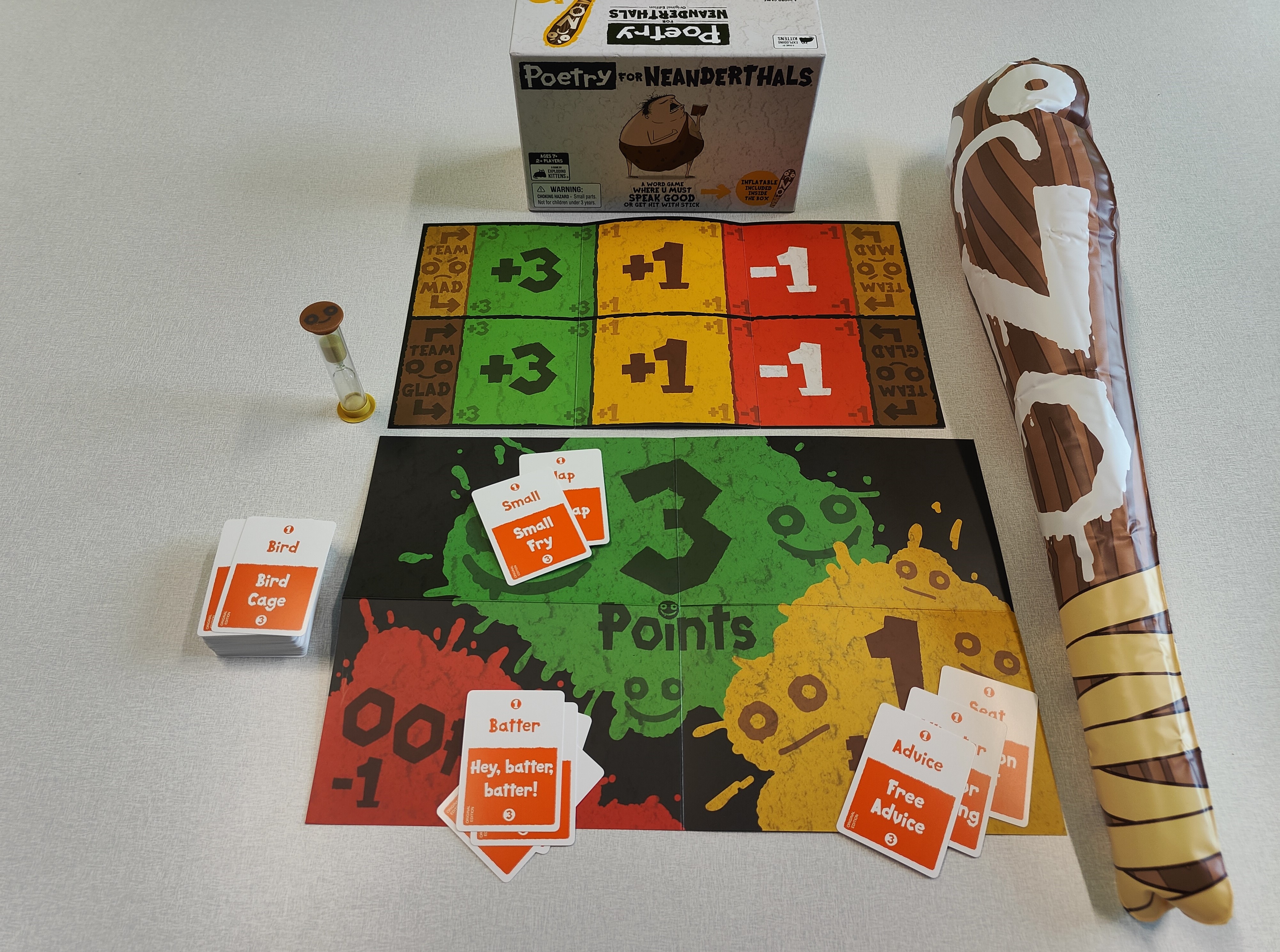 Poetry for Neanderthals box, 2 game mats, sand timer, stack of cards, and inflatable "NO" bat