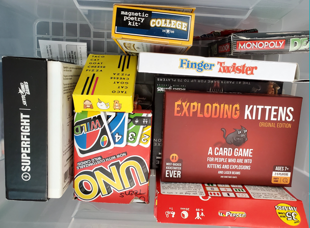 Board games in a box, from the left: Superfight, Uno, Taco Cat Goat Cheese Pizza, Magnetic Poetry kit: College, Finger Twister, Monopoly Deals, Exploding Kittens, and Set
