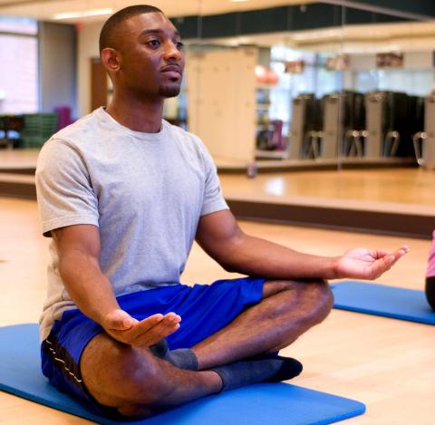 Man seated cross legged, hands down, palms up.  