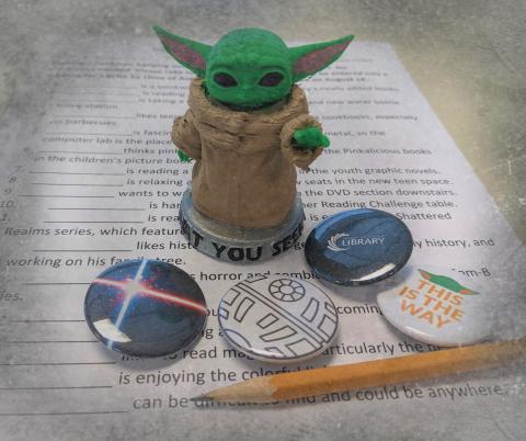 Baby Yoda figurine, light sword button, Death Star button, vector button, and Baby Yoda button on form, pencil