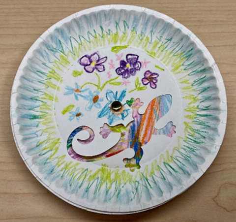 Paper plate with a lizard shaped hole showing color of picture underneath.