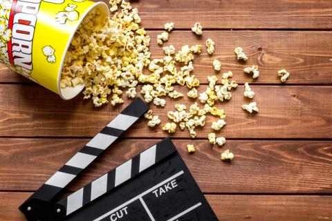 A bucket of popcorn is spilled across a wooden background next to a clapperboard