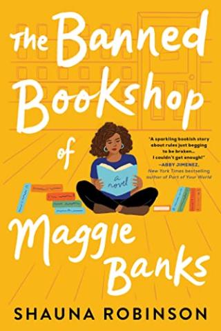 The book cover of "The Banned Bookshop of Maggie Banks." The cover is yellow with a cartoon women reading a blue book. She is surrounded by stacks of books to her left and right. 