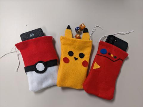 Pokeball drawstring bag with powerband inside, Pikachu drawstring bag with dice, and Pokedex drawstring bag with cell phone inside