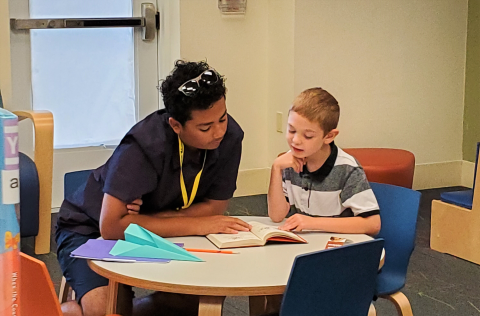 Teen volunteer mentor and child reading together