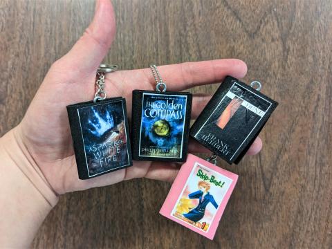 hand holding mini book charms of A Spark of White Fire, Golden Compass, Dune and Skip Beat volume 1