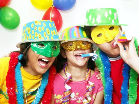 Three children dressed in masks and celebratory hats.