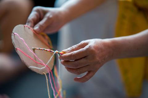 A person using cardboard to make a friendship bracelet.