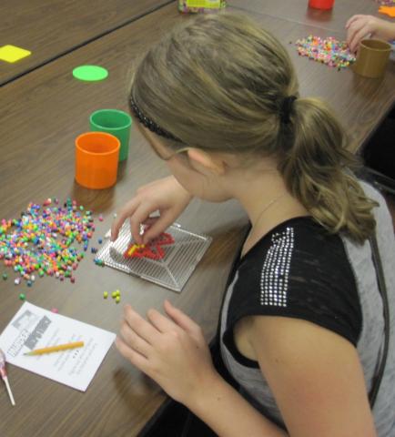 Teen with hair pulled back in a pony tail carefully places beads on a pegboard