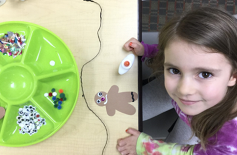 a child looking up from a table holding craft supplies