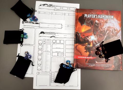 To the right: Dungeons and Dragons Players Handbook, a black bag of dice on top of the book, to the left there are 3 blank characters sheets and 4 black bags with colorful Dungeons and Dragons dice spilling out