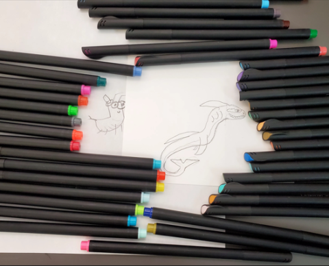 Two drawings by teens: one to the left of a cricket, one to the right of a dragon with colorful pens surrounding them.