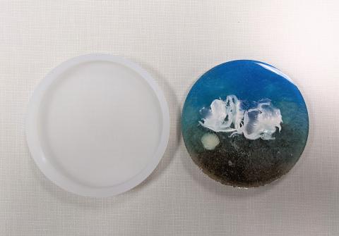 Resin coaster decorated with sand, shell, and color.