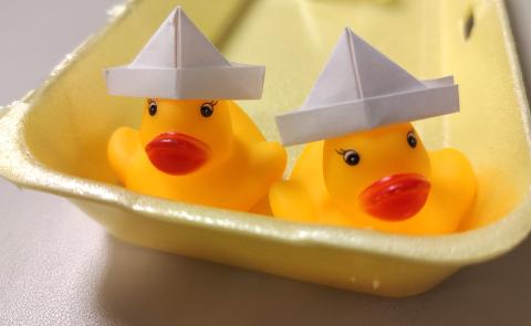2 yellow rubber ducks with white paper hats in a yellow egg carton