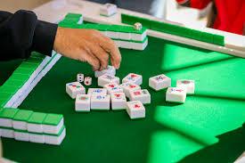 Mahjong tiles on green felt background with player placing a discard tile