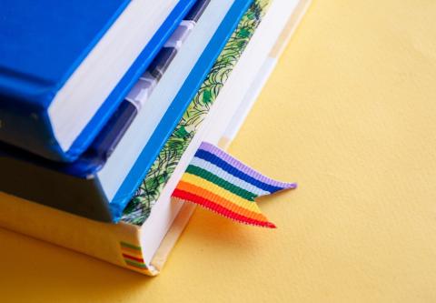 A stack of three books on a table with a rainbow bookmark
