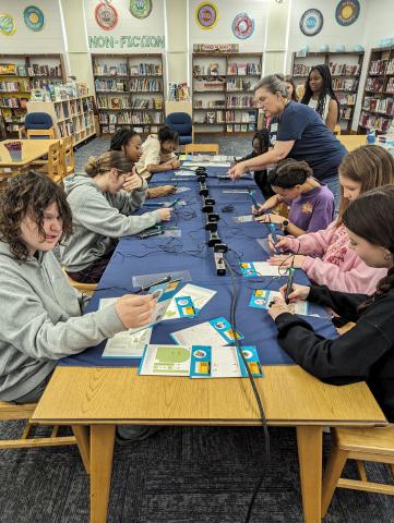 A group of teens at a long table using 3D pens