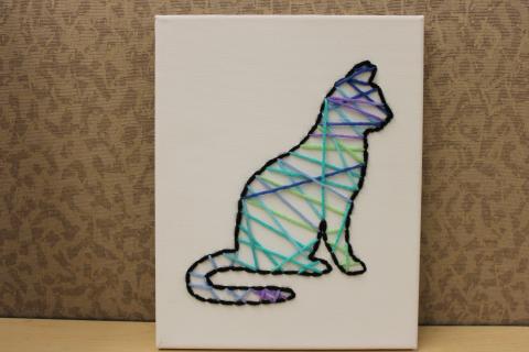 Outline of cat embroidered in black yarn on a white canvas. Multicolor yarn fills in the middle.