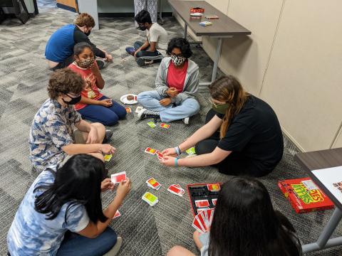 Teens sitting on the floor playing a card game.