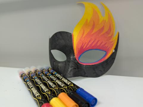 Costume mask colored in black with flames, and a set of acrylic paint pens.