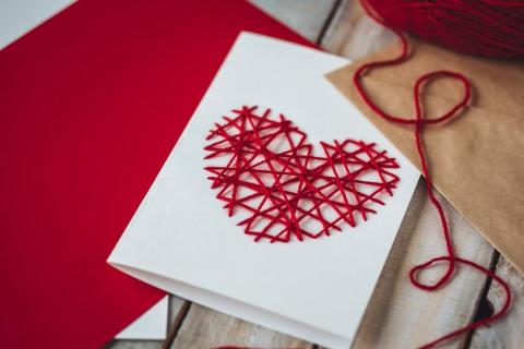 A white card with red thread crisscrossing in the shape of a heart. 