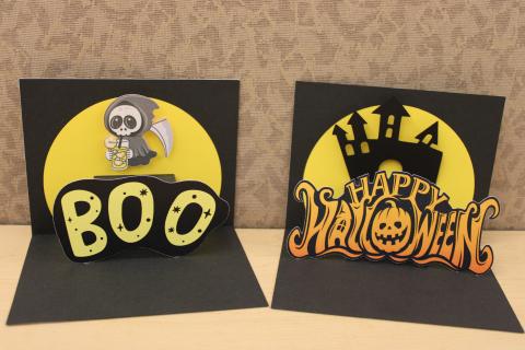 two Halloween pop up cards. one with Boo text and a grim reaper drinking lemonade and the other with Happy Halloween text with a haunted house in the background.