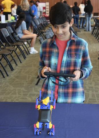 Boy in checkered shirt using an iPad to make Petoi robot dog move.