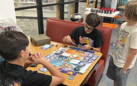 Three teen boys playing the Pokemon card game.