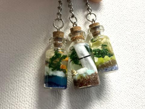 3 mini bottle charms with colored sand, gravel, and plant bits