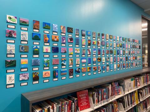 dozens of tiny canvas paintings displayed on a wall in a grid formation