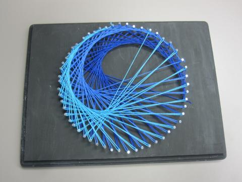 Three shades of blue threads stringed across nails in round shape on a black board