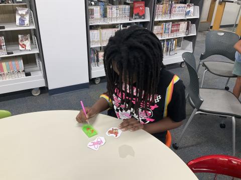 Teen with black hair wearing a black shirt sits at a table and works on a Diamond Painting project