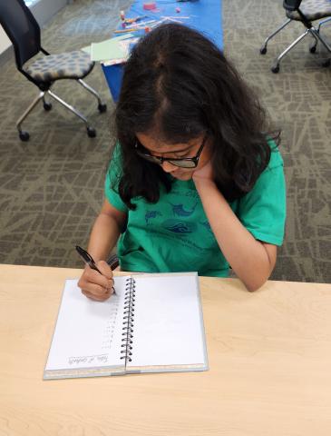 A girl wearing a green shirt is writing in a journal.